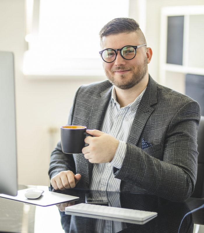 Portrait of successful entrepreneur drinking coffee and using computer at cozy home office